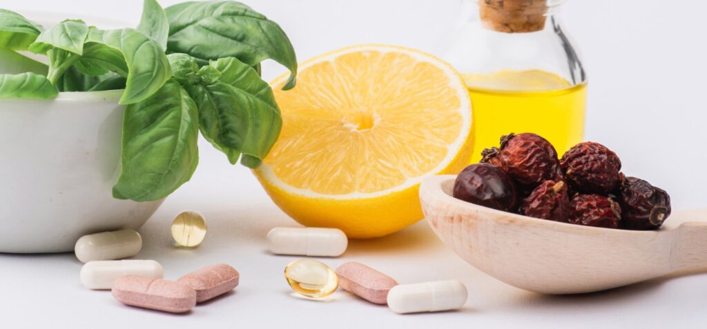 Green leaves in mortar, berries and lemon near pills on white background