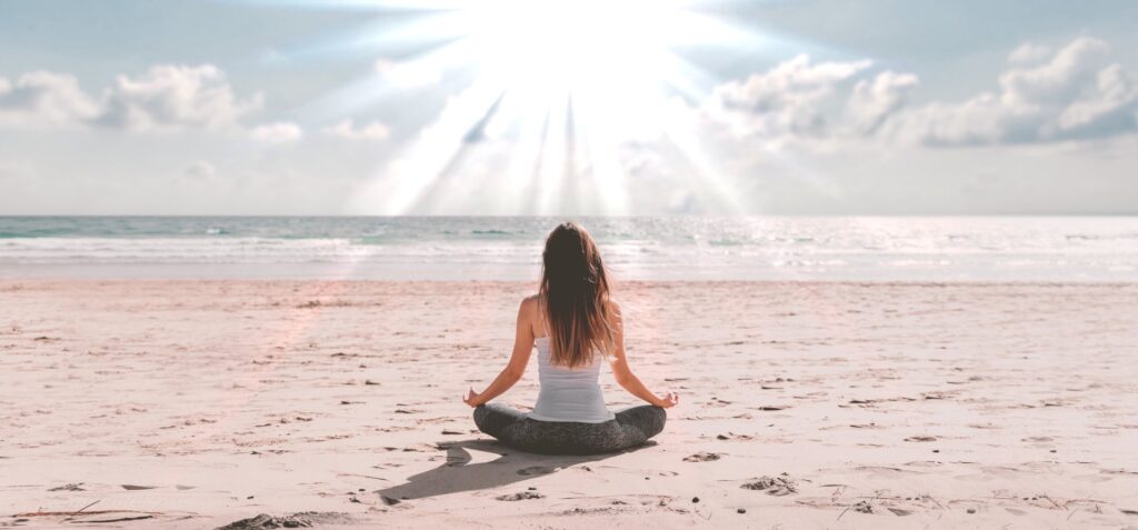 Woman meditating on beach infront of the sun